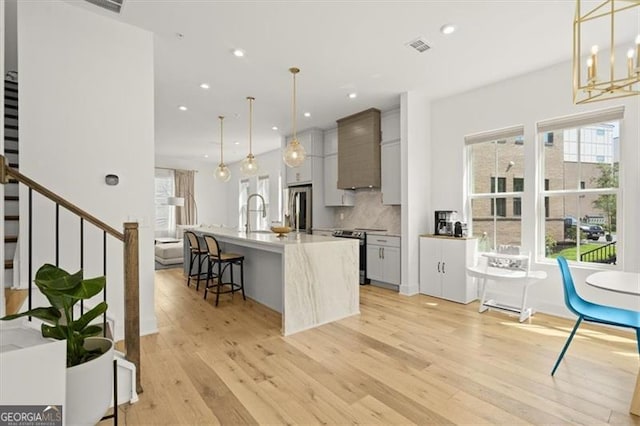 kitchen with light hardwood / wood-style flooring, appliances with stainless steel finishes, a kitchen island with sink, and hanging light fixtures