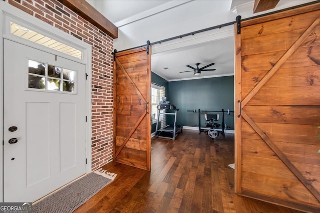 entryway with dark wood-type flooring, a barn door, ornamental molding, ceiling fan, and brick wall