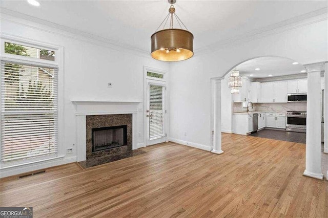 unfurnished living room featuring ornamental molding, a fireplace, light hardwood / wood-style flooring, and decorative columns