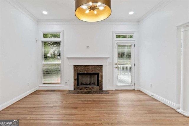 unfurnished living room featuring a wealth of natural light, a high end fireplace, light hardwood / wood-style floors, and crown molding