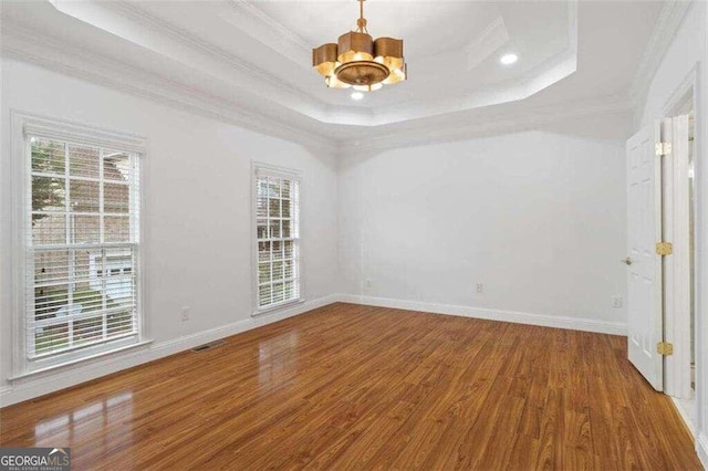 empty room with an inviting chandelier, a tray ceiling, hardwood / wood-style floors, and ornamental molding