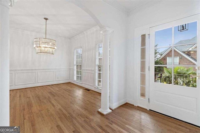 entrance foyer featuring wood-type flooring, a healthy amount of sunlight, ornate columns, and a chandelier