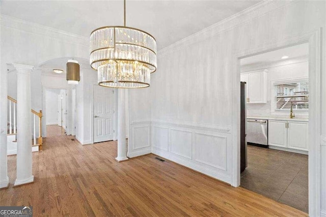 unfurnished dining area featuring an inviting chandelier, wood-type flooring, ornate columns, and crown molding