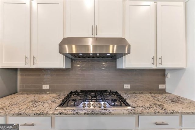 kitchen featuring light stone counters, stainless steel gas cooktop, decorative backsplash, wall chimney range hood, and white cabinetry