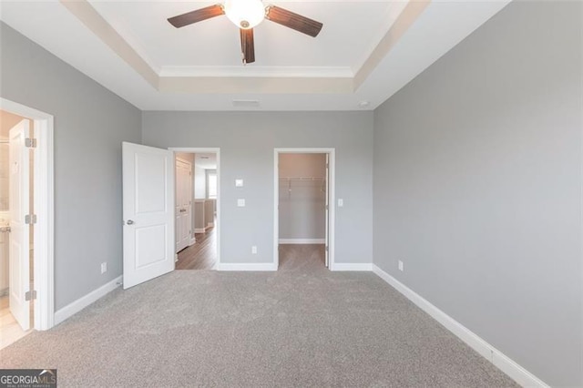 unfurnished bedroom featuring a tray ceiling, a walk in closet, light carpet, and ceiling fan