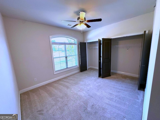 unfurnished bedroom featuring light carpet, ceiling fan, and multiple closets