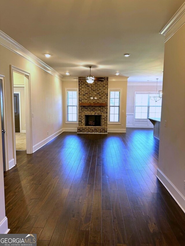 unfurnished living room featuring dark hardwood / wood-style flooring, a brick fireplace, crown molding, and plenty of natural light