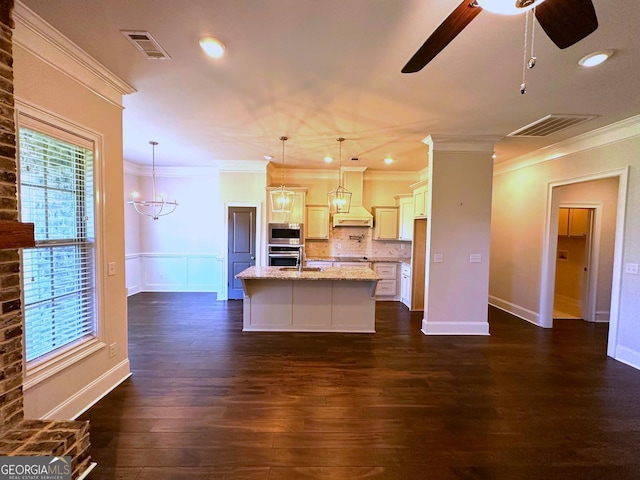 kitchen with premium range hood, light stone counters, decorative light fixtures, stainless steel appliances, and a kitchen island with sink