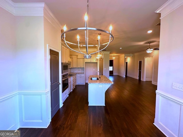 kitchen featuring stainless steel microwave, light stone counters, wall oven, a center island with sink, and decorative light fixtures