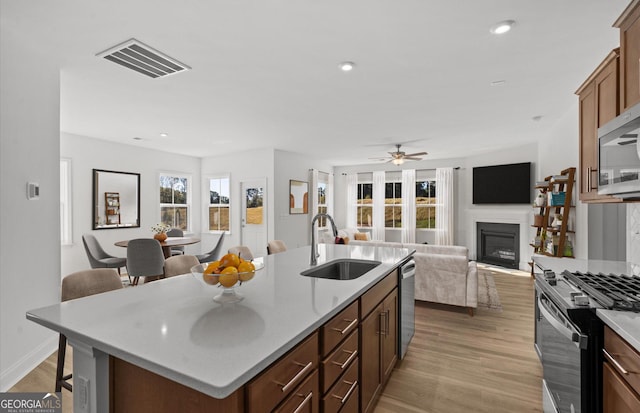 kitchen with a kitchen bar, stainless steel appliances, a kitchen island with sink, sink, and light hardwood / wood-style flooring