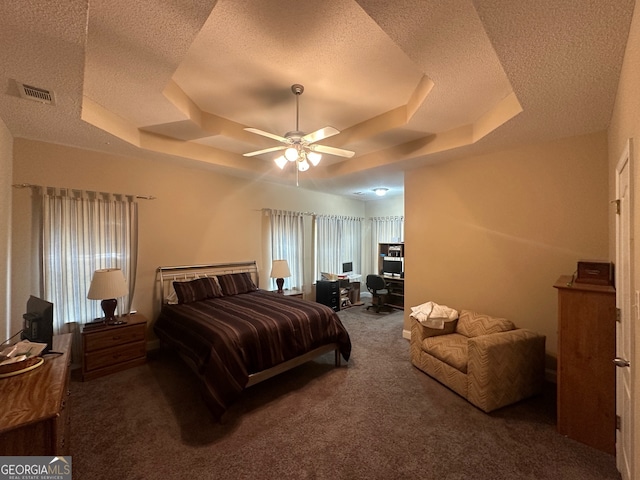 bedroom with ceiling fan, a tray ceiling, a textured ceiling, and dark carpet