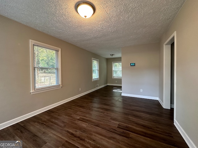 empty room with a textured ceiling, dark hardwood / wood-style floors, and plenty of natural light