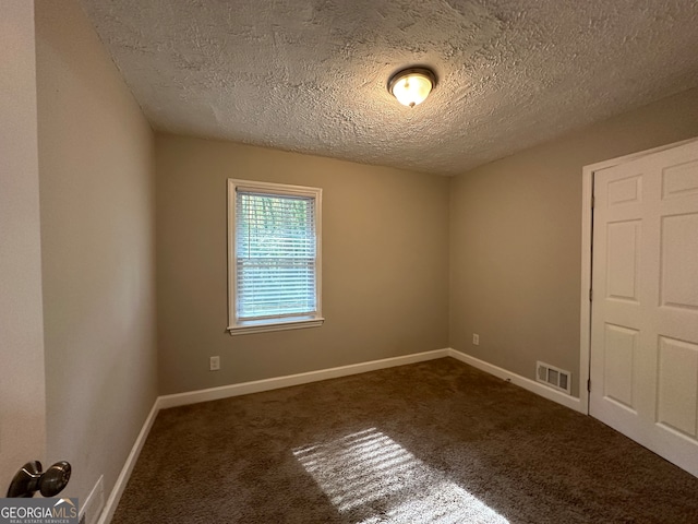 unfurnished room featuring dark colored carpet and a textured ceiling