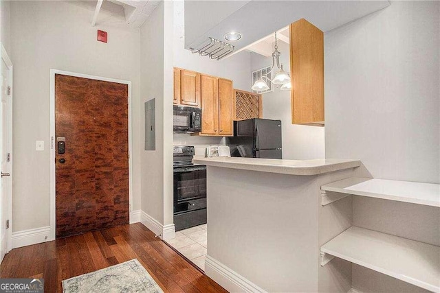 kitchen featuring kitchen peninsula, hanging light fixtures, black appliances, a kitchen breakfast bar, and light wood-type flooring