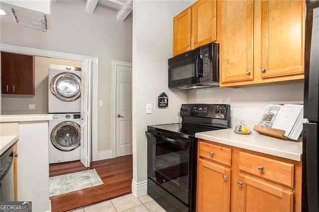 kitchen with stacked washer and dryer, black appliances, light tile patterned floors, and beam ceiling