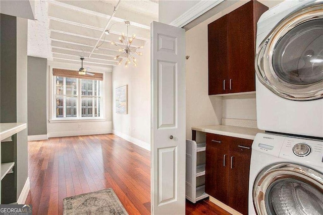 washroom featuring dark wood-type flooring, stacked washer and clothes dryer, cabinets, and ceiling fan with notable chandelier