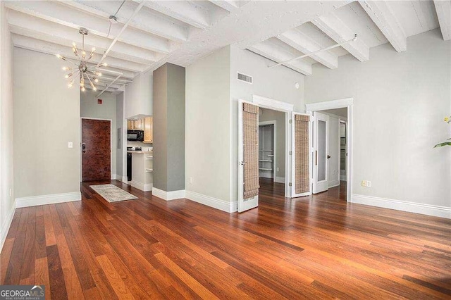 unfurnished living room with beamed ceiling, a chandelier, hardwood / wood-style flooring, and a towering ceiling