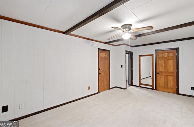 unfurnished bedroom featuring wood walls, ceiling fan, beam ceiling, and light carpet