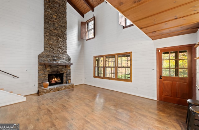 unfurnished living room with wood-type flooring, a stone fireplace, high vaulted ceiling, wood walls, and wooden ceiling