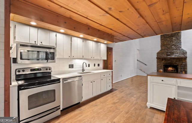 kitchen featuring stainless steel appliances, white cabinets, sink, a fireplace, and light wood-type flooring