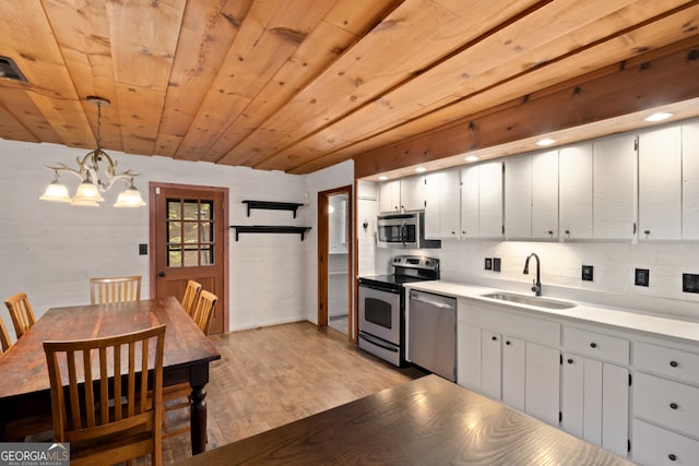 kitchen with stainless steel appliances, decorative light fixtures, wood walls, sink, and light hardwood / wood-style floors