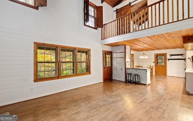 unfurnished living room with high vaulted ceiling, an inviting chandelier, wood ceiling, and hardwood / wood-style floors