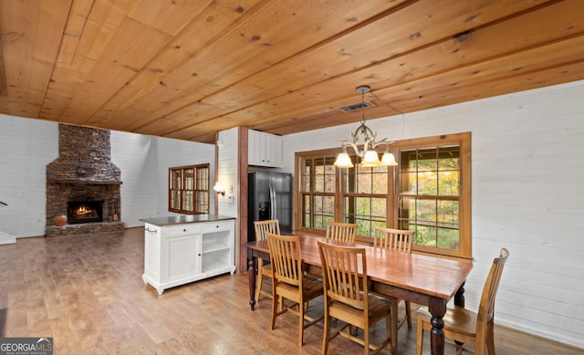 dining space featuring wooden ceiling, light hardwood / wood-style floors, a stone fireplace, and a notable chandelier