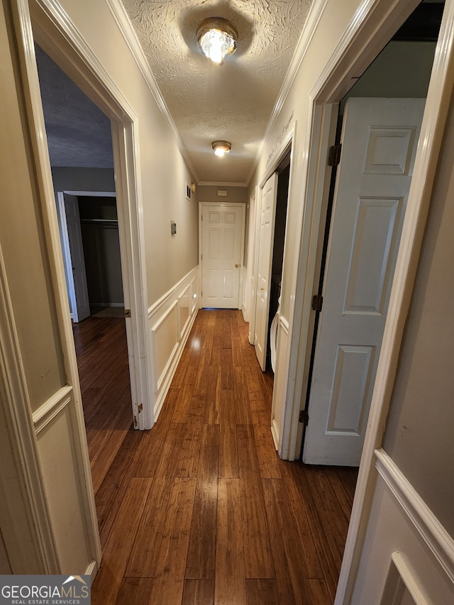 hall with dark hardwood / wood-style floors, ornamental molding, and a textured ceiling