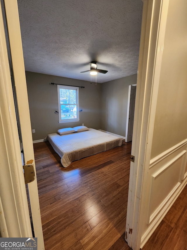 unfurnished bedroom with a textured ceiling, ceiling fan, and dark wood-type flooring