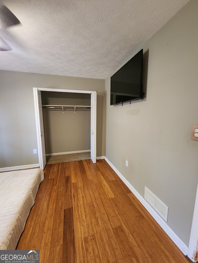 unfurnished bedroom featuring hardwood / wood-style flooring, a textured ceiling, and a closet