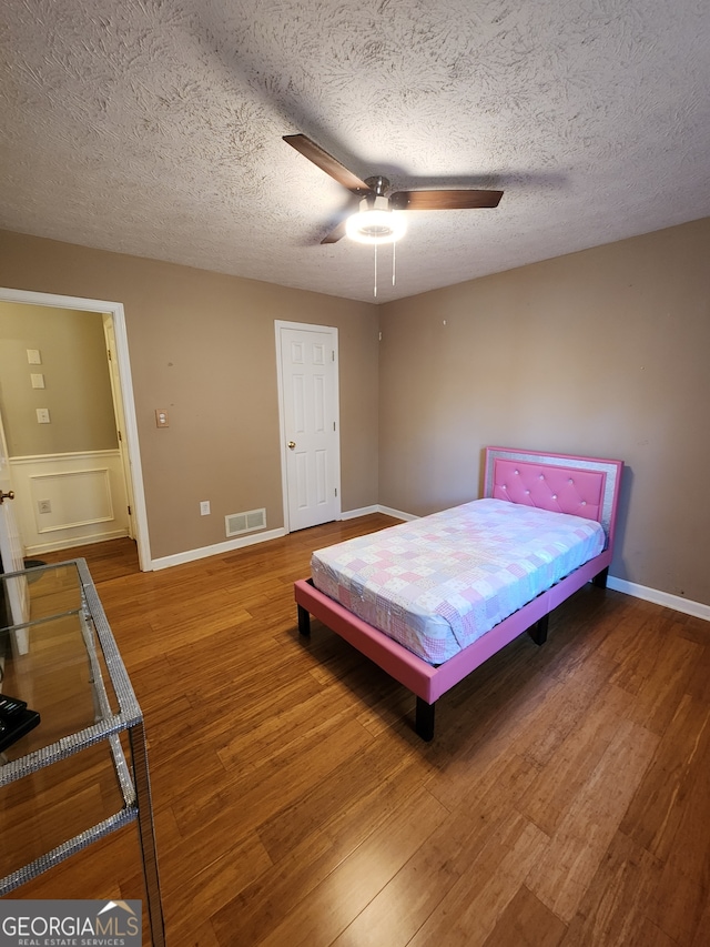 bedroom with hardwood / wood-style flooring, ceiling fan, and a textured ceiling