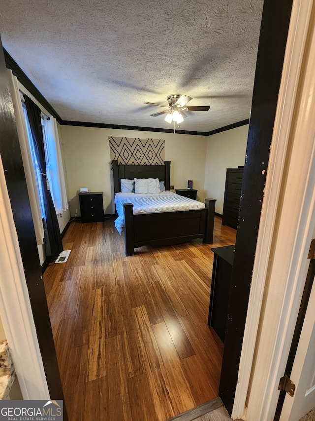 unfurnished bedroom with wood-type flooring, a textured ceiling, ceiling fan, and crown molding