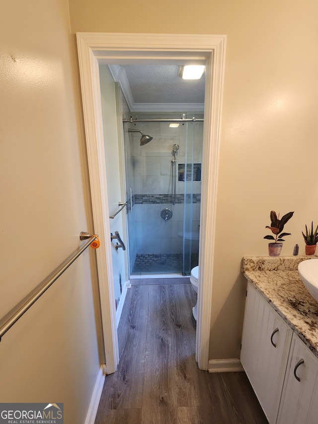 bathroom featuring vanity, wood-type flooring, crown molding, a textured ceiling, and a shower with shower door