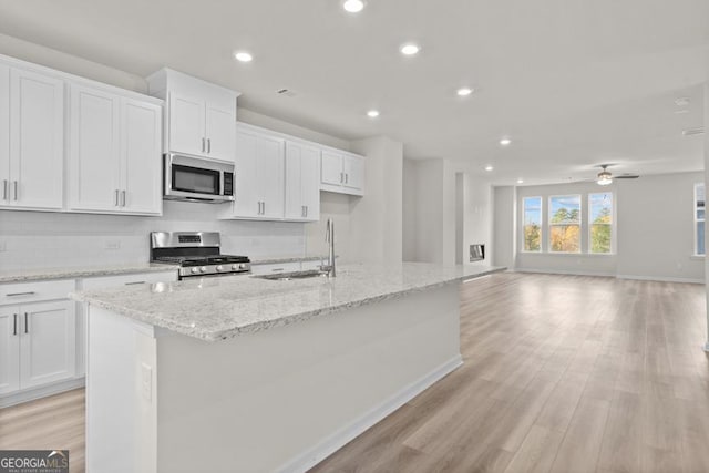 kitchen featuring stainless steel appliances, white cabinetry, ceiling fan, and a center island with sink