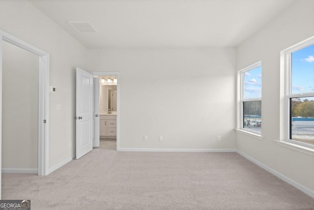 unfurnished bedroom featuring ensuite bathroom, multiple windows, and light colored carpet