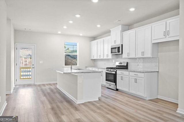 kitchen featuring a kitchen island with sink, white cabinetry, stainless steel appliances, and light stone counters