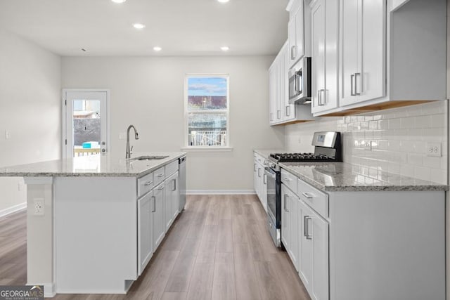 kitchen with sink, light stone countertops, an island with sink, white cabinetry, and stainless steel appliances