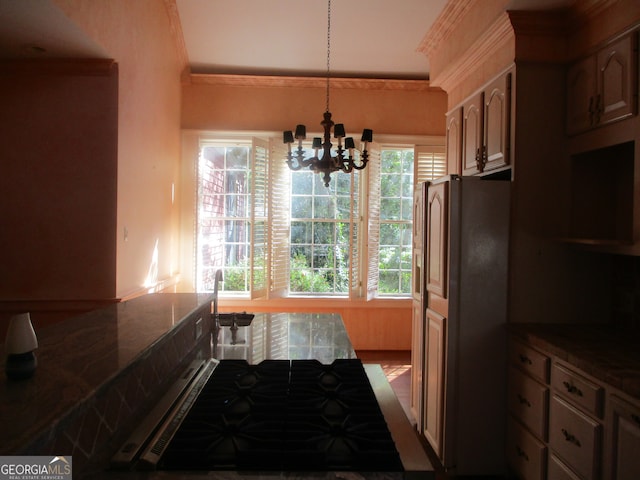 kitchen featuring a chandelier, a wealth of natural light, stainless steel refrigerator, and ornamental molding