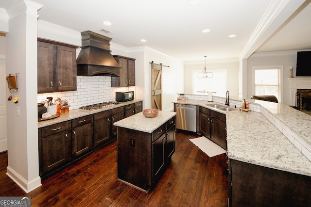 kitchen with sink, stainless steel appliances, a barn door, pendant lighting, and a kitchen island with sink