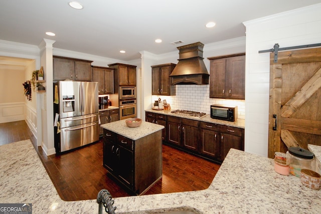 kitchen featuring light stone counters, appliances with stainless steel finishes, a kitchen island, custom exhaust hood, and ornamental molding