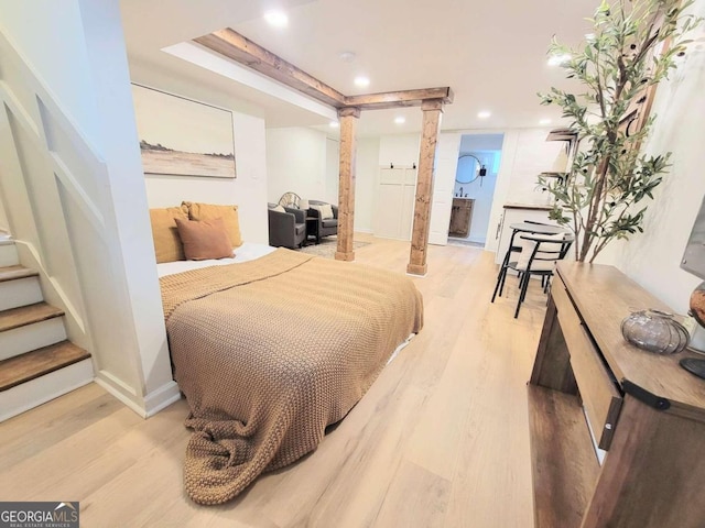 bedroom with ensuite bathroom, decorative columns, a tray ceiling, and light hardwood / wood-style flooring