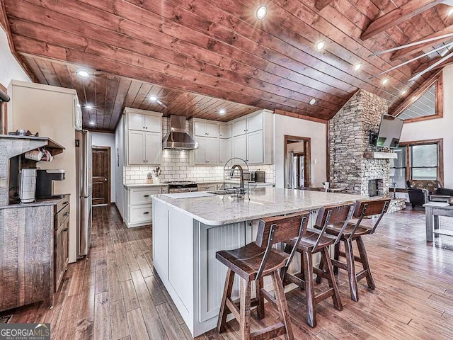 kitchen with light stone counters, white cabinets, hardwood / wood-style floors, wall chimney exhaust hood, and wooden ceiling