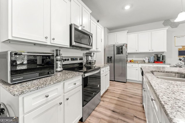 kitchen featuring white cabinetry, light wood-type flooring, appliances with stainless steel finishes, and hanging light fixtures