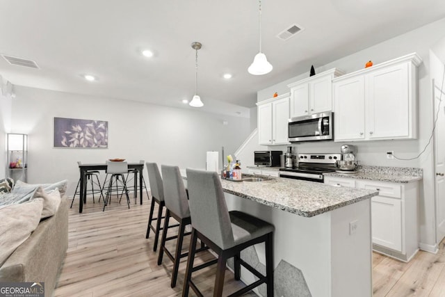 kitchen featuring stainless steel appliances, white cabinets, pendant lighting, and light wood-type flooring