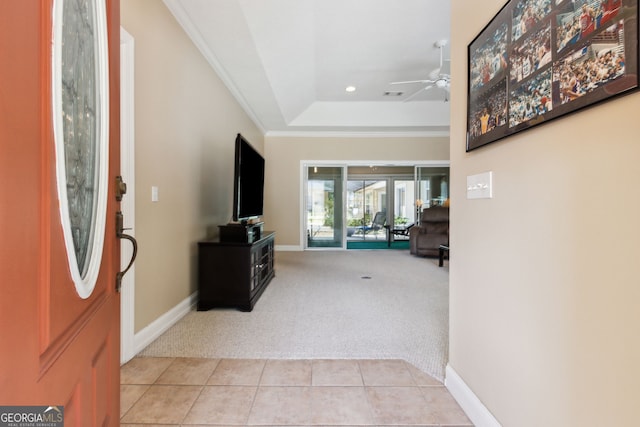 foyer featuring crown molding, a raised ceiling, light carpet, and ceiling fan