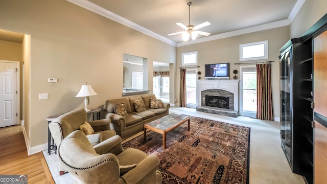 living room with a high ceiling, a stone fireplace, light hardwood / wood-style flooring, ceiling fan, and ornamental molding