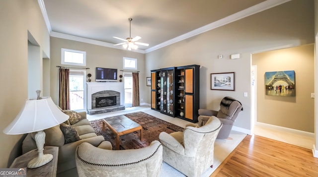 living room featuring ceiling fan, a fireplace, ornamental molding, and light wood-type flooring