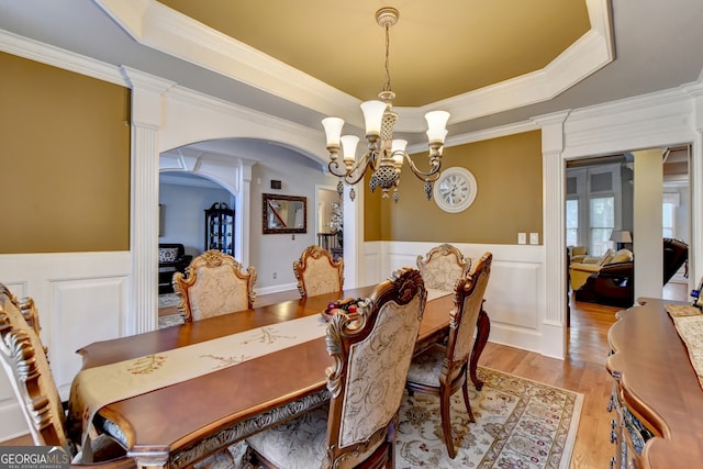 dining space with ornamental molding, light hardwood / wood-style flooring, a notable chandelier, and a tray ceiling