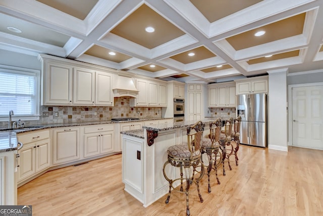 kitchen featuring light stone counters, a kitchen island, appliances with stainless steel finishes, sink, and custom exhaust hood