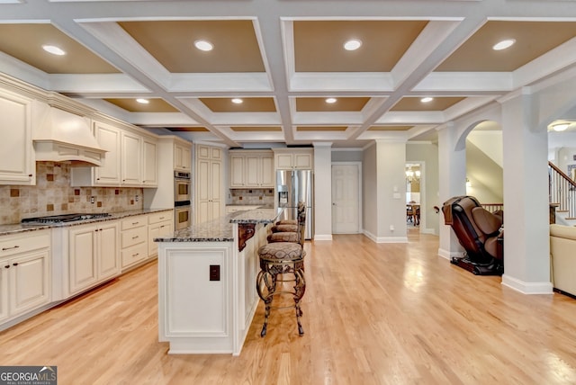 kitchen with cream cabinets, a breakfast bar area, stone counters, a center island, and premium range hood